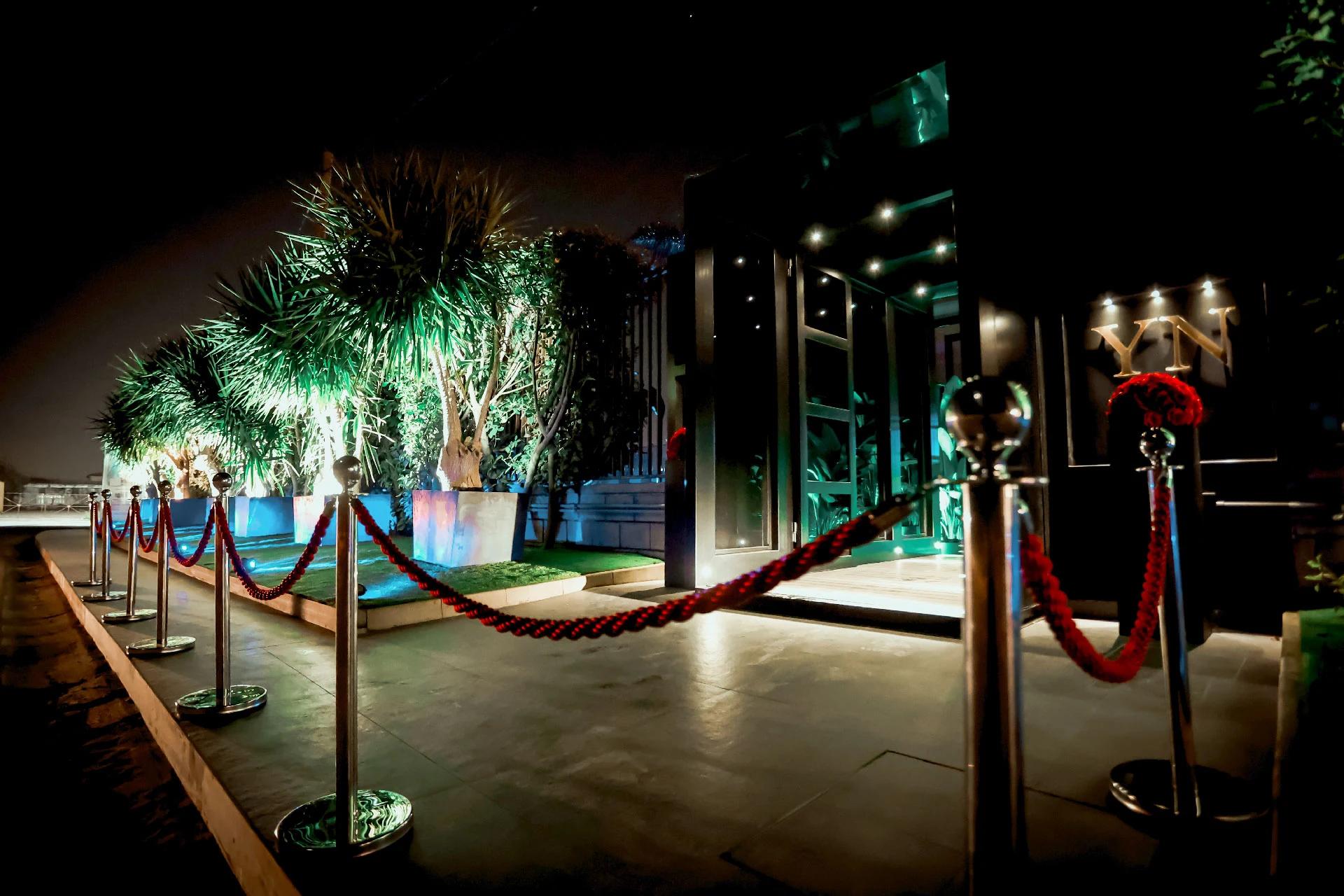 Ingresso YOLO illuminato, palme e tappeto rosso